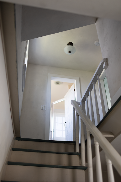 Interior stair landing looking up toward a ceiling fixture and original banister