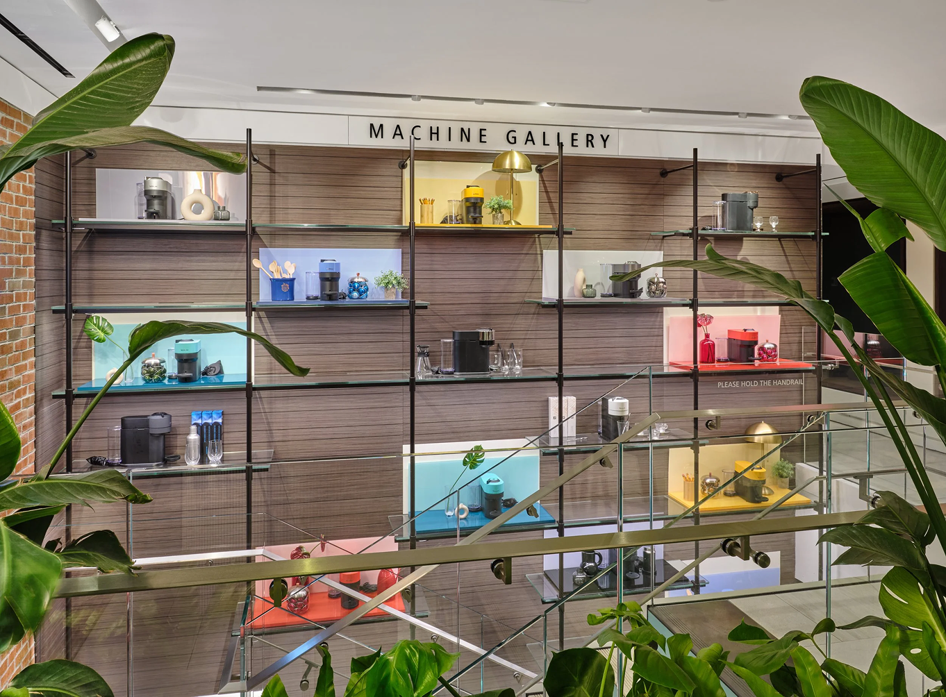 Machine Gallery — floor-to-ceiling shelving framing the full Vertuo Pop color story through tropical foliage
