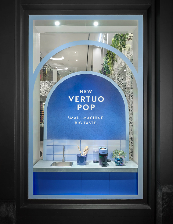 Vertuo Pop retail window — blue arch with the New Vertuo Pop, Small Machine. Big Taste. lockup framing a kitchen-counter vignette